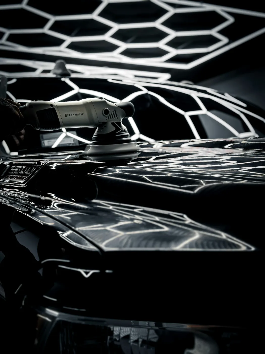 A detailer machine-polishing a black car under hexagon studio lights