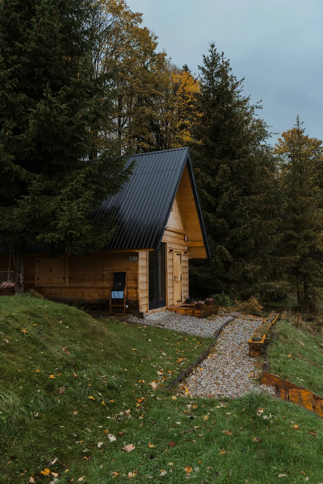 A timber cabin with a dark metal roof and a gravel path through a green lawn