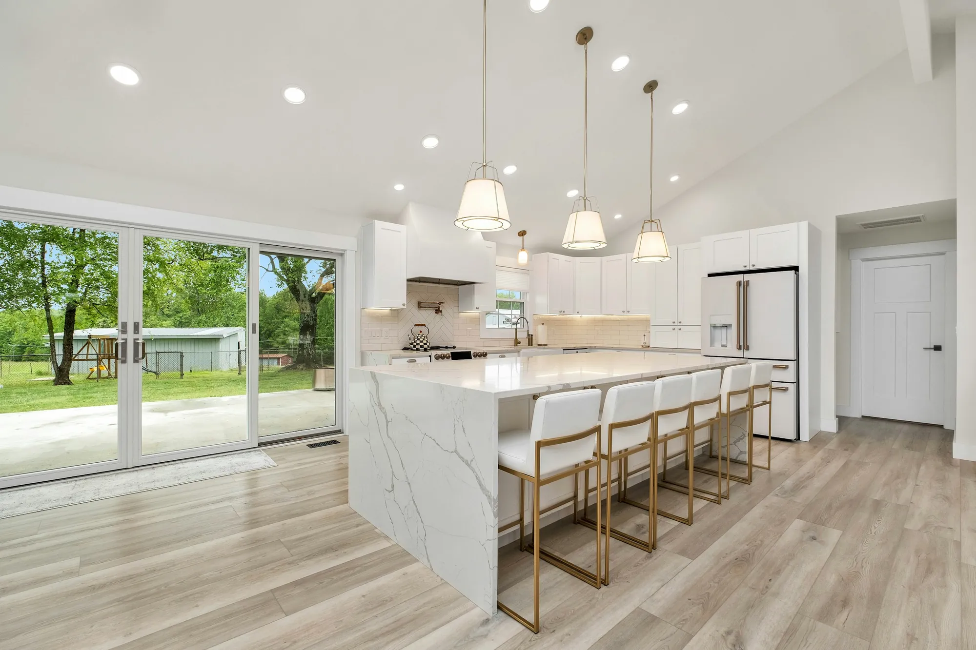 A bright renovated kitchen with a marble island, pendant lights and wood floors