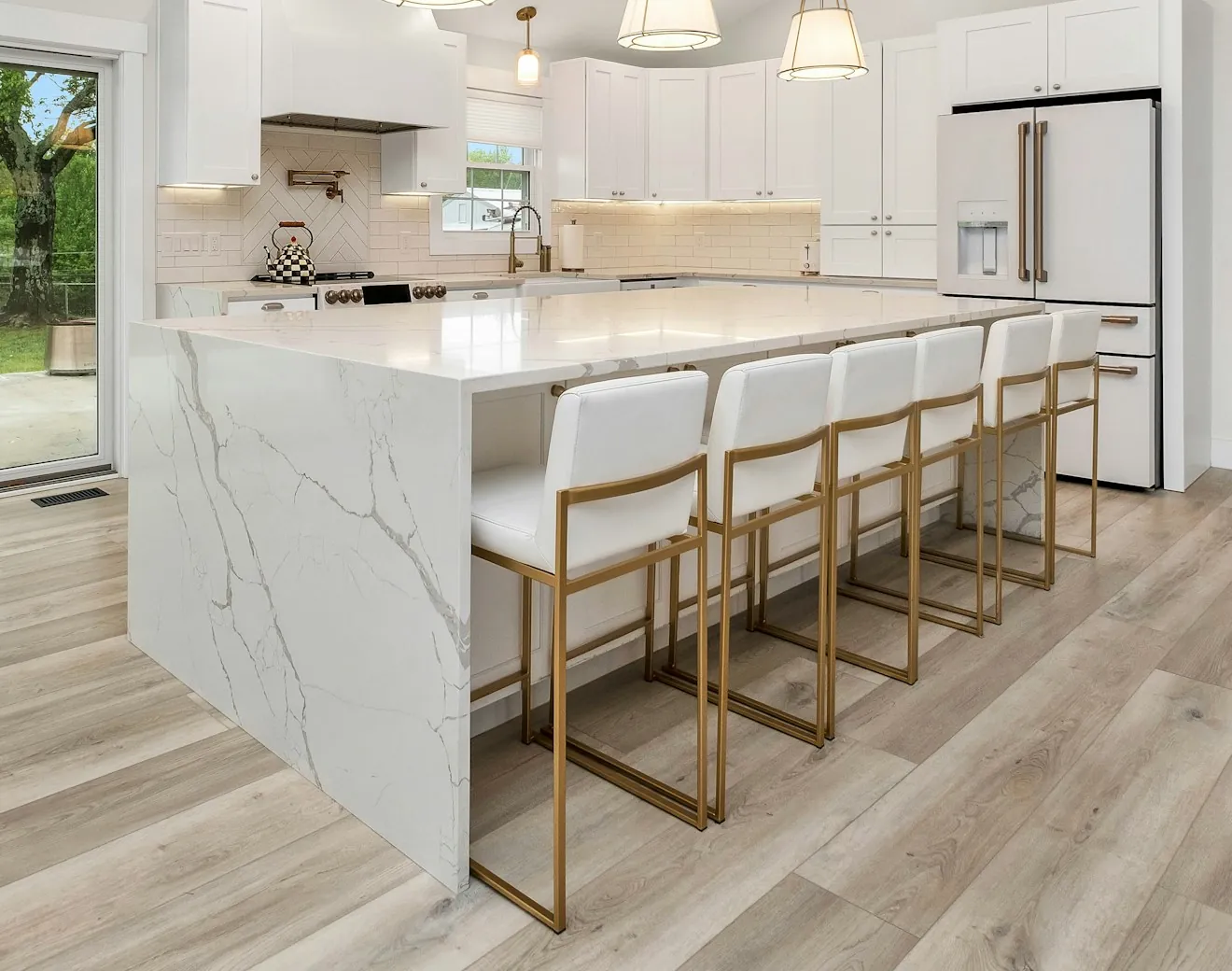 A marble kitchen island with white bar stools and brass legs